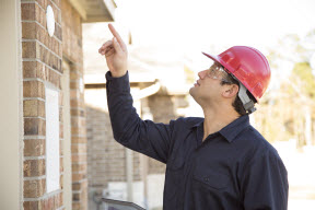 Man and red hard hat looking at the gutters of a home