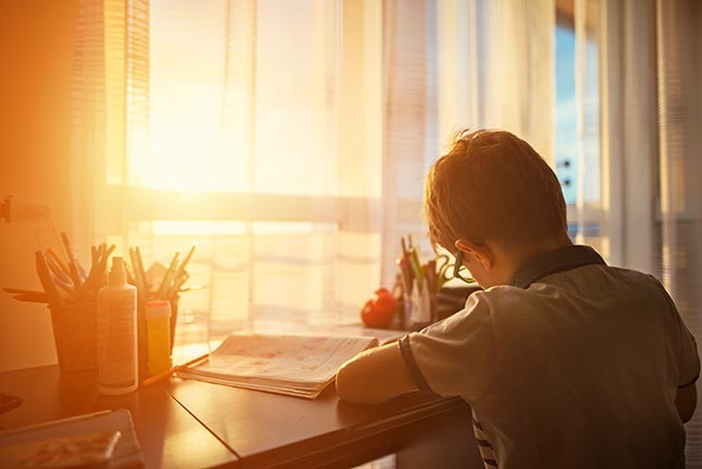 A child doing homework in bedroom in front of window