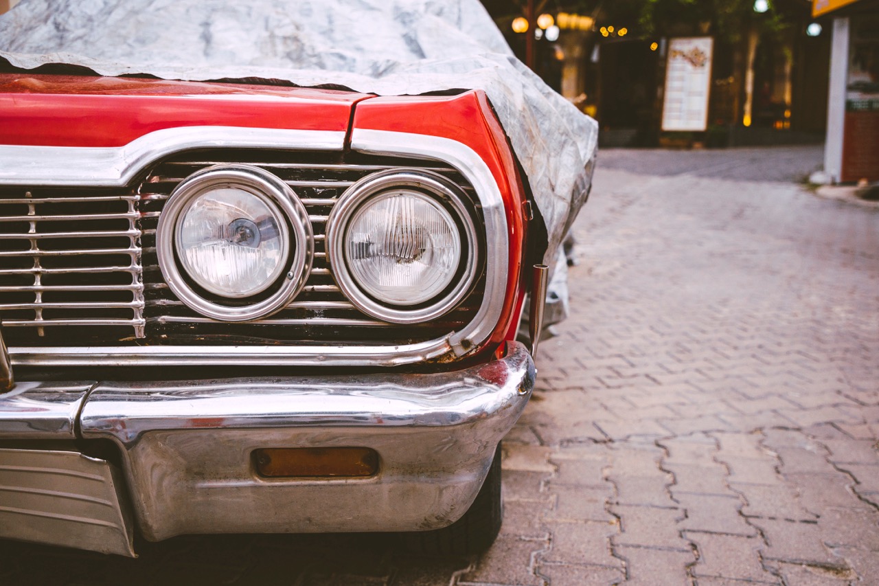 Nose of a red classic car with tarp pulled back